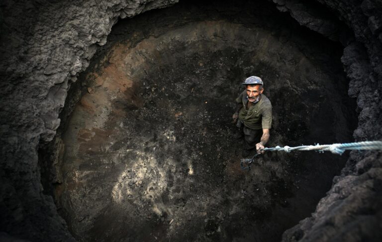 A man stands in a deep pit holding a rope, looking up from a high angle view.